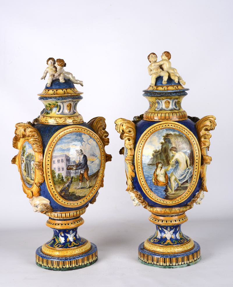 Coppia di vasi in maiolica policroma prese laterali a figlia, coperchio con putti, scene figurate...